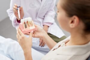 Woman holds model of dental implant with dentist pointing to it.